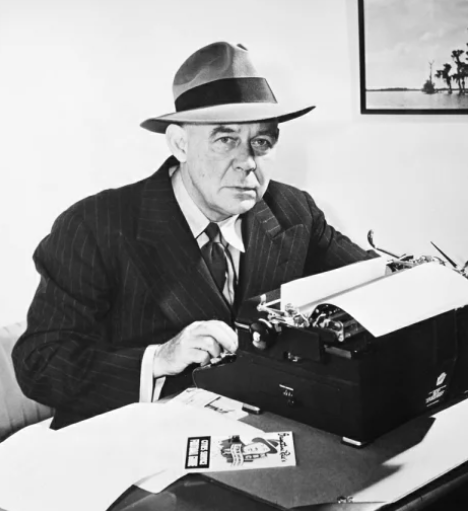 Grantland Rice in a fedora, typing at his desk