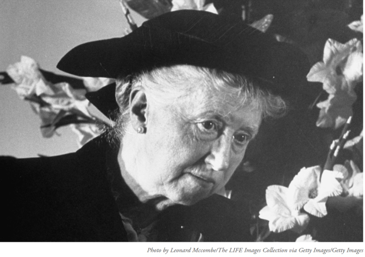 Marianne Moore in a dark hat, surrounded by flowers
