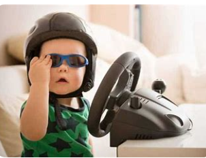 A toddler in a helmet and sunglasses at a toy steering wheel