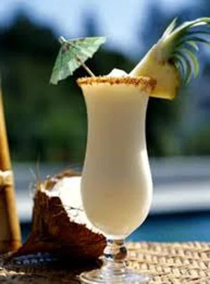 A piña colada with a pineapple slice and paper umbrella, beside a coconut